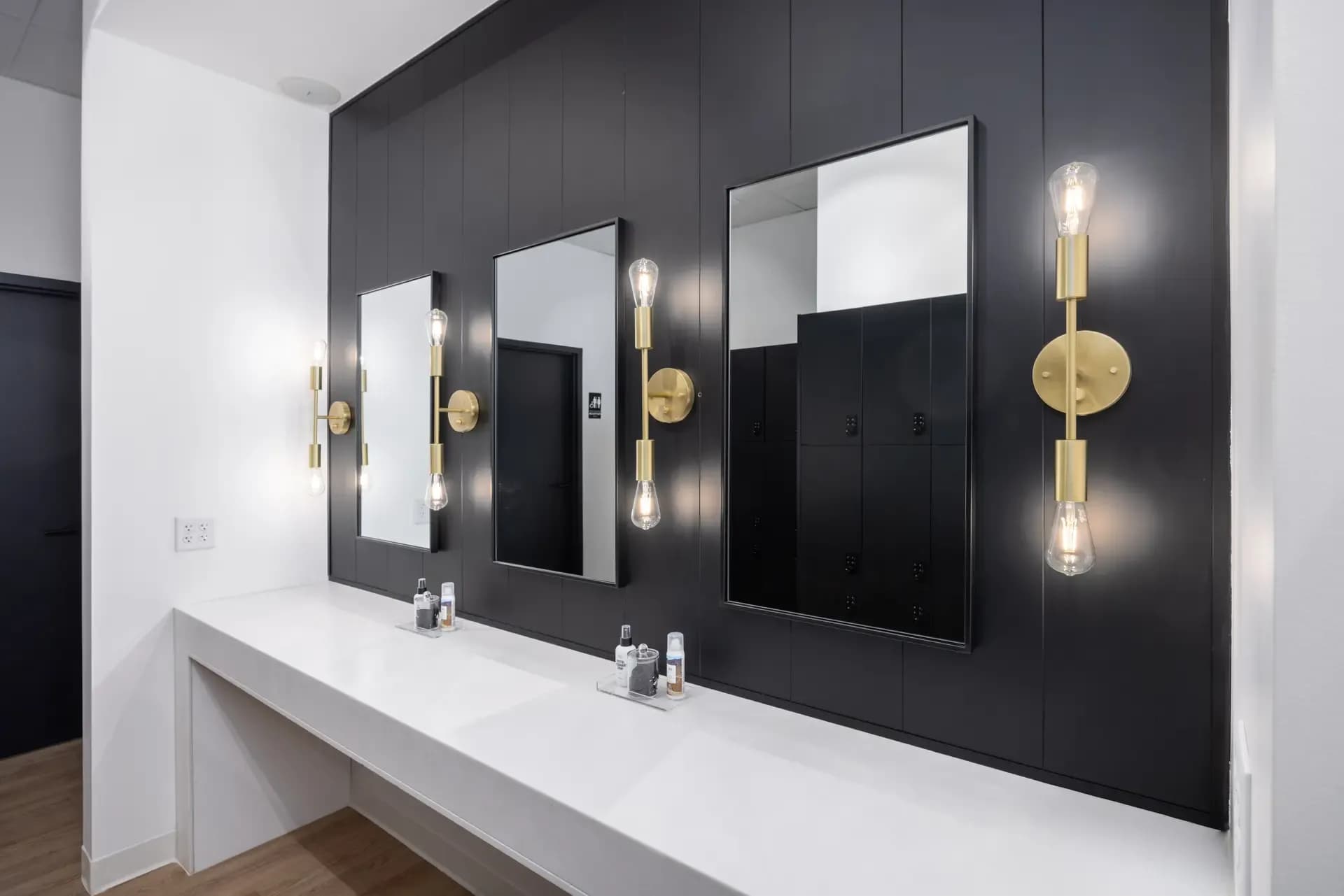 Modern Pvolve studio vanity area with mirrors, black paneling, and brass lighting
